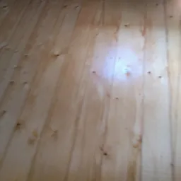 Jasne deski podłogowe z widocznymi sękami, ułożone pionowo, oświetlone od góry.