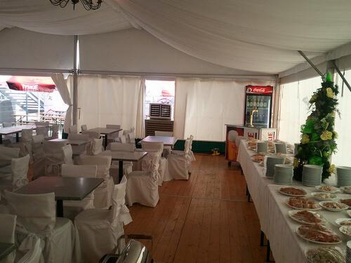 Wnętrze namiotu bankietowego w Gorzowie Wielkopolskim z klimatyzacją, stoły i krzesła w białych pokrowcach, bufet z jedzeniem i napojami, dekoracyjna choinka.