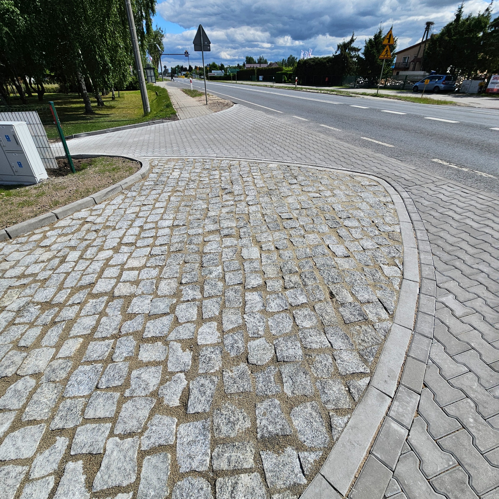 Nawierzchnia z kostki granitowej ułożona na parkingu, oddzielona obrzeżem od chodnika z szarej kostki betonowej i asfaltowej drogi. Widok z góry na gotowe podłoże.