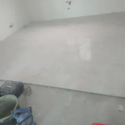 Ułożone jasnoszare płytki podłogowe w nowo wykończonym pomieszczeniu, widoczne narzędzia glazurnicze i wiadro z zaprawą w rogu.