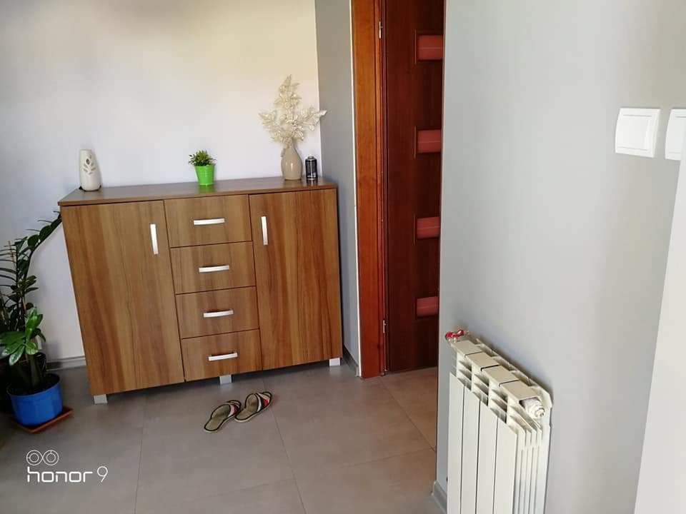 Nowoczesna komoda z drewnianymi frontami, ustawiona w przedpokoju z szarymi ścianami, obok grzejnika i drewnianych drzwi.