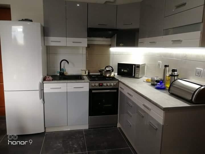 Wykończona kuchnia w odcieniach szarości i bieli w Opocznie, z oświetleniem LED podszafkowym i czarną armaturą, widok na zabudowę kuchenną z lodówką, piekarnikiem i mikrofalówką.