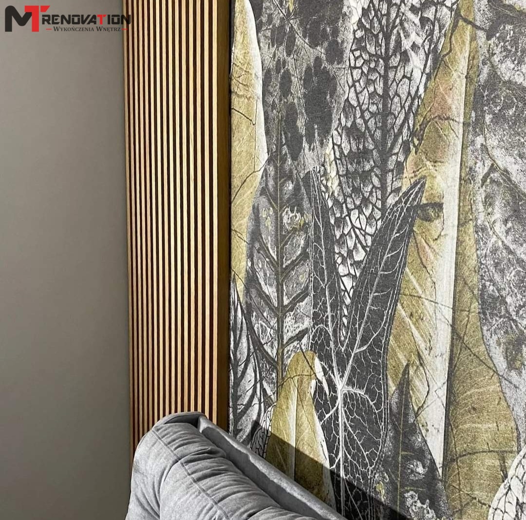 Dekoracyjna ściana z drewnianymi lamelami i tapetą w motywie liści, widoczny fragment szarej sofy.