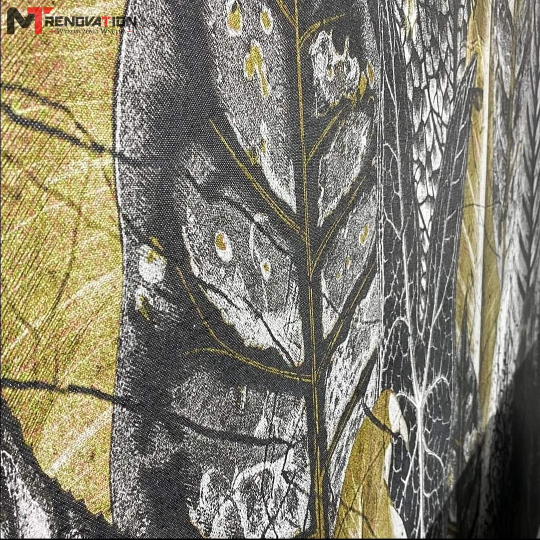 Wzorzysta tapeta z motywem liści w odcieniach szarości, bieli i złota, zainstalowana w Olsztynie, o wyraźnej strukturze tkaniny i widocznym logo firmy na górze.