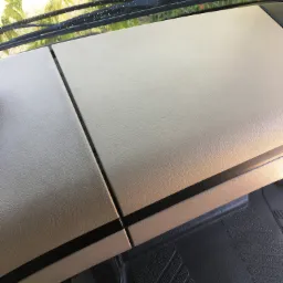 Wnętrze kabiny pojazdu z widoczną deską rozdzielczą i przednią szybą z kroplami wody, liście drzew widoczne przez szybę.