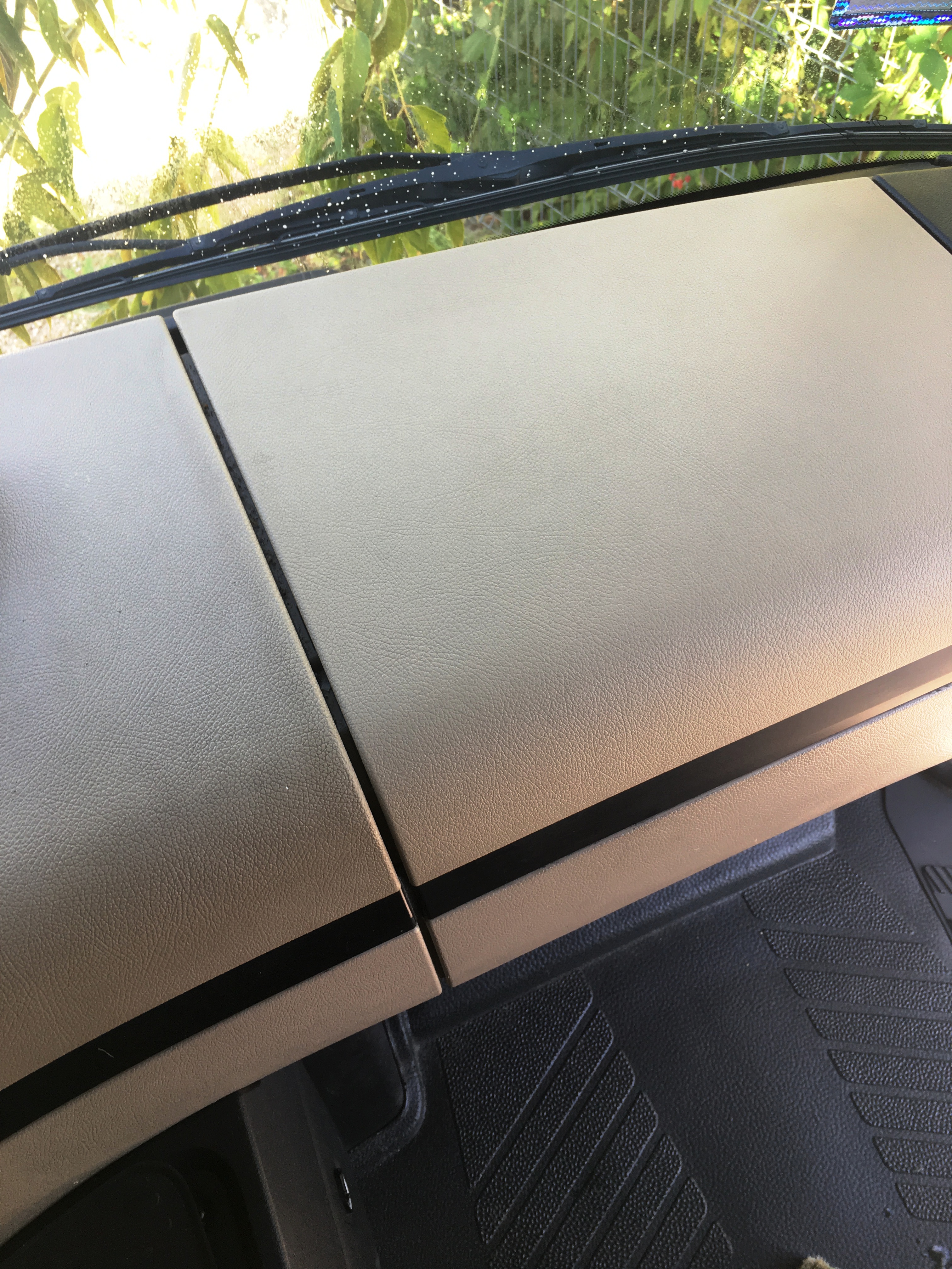 Wnętrze kabiny pojazdu z widoczną deską rozdzielczą i przednią szybą z kroplami wody, liście drzew widoczne przez szybę.