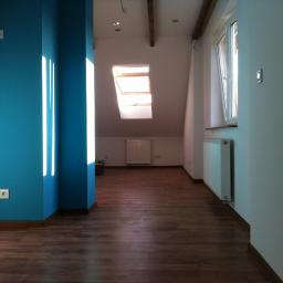 Awis Finishing - Poddasze po remoncie: turkusowa ściana z promieniami słońca kontrastuje z drewnianą podłogą i białymi ścianami, widoczne okno dachowe i grzejniki.