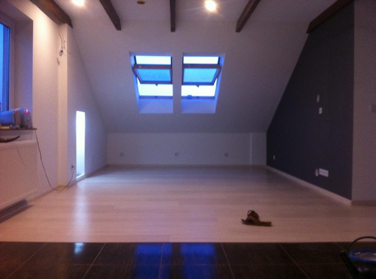 Poddasze po remoncie w Zawadzie z jasną podłogą, dwoma oknami dachowymi i ciemnoszarą ścianą akcentującą.