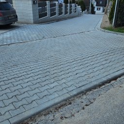 ŁUKASZ ŁOZOWSKI USŁUGI KOPARKĄ - Szeroki kadr na ulicę w Sulechowie wyłożoną szarą kostką brukową w jodełkę, z widocznymi domami jednorodzinnymi i ogrodzeniami w tle.