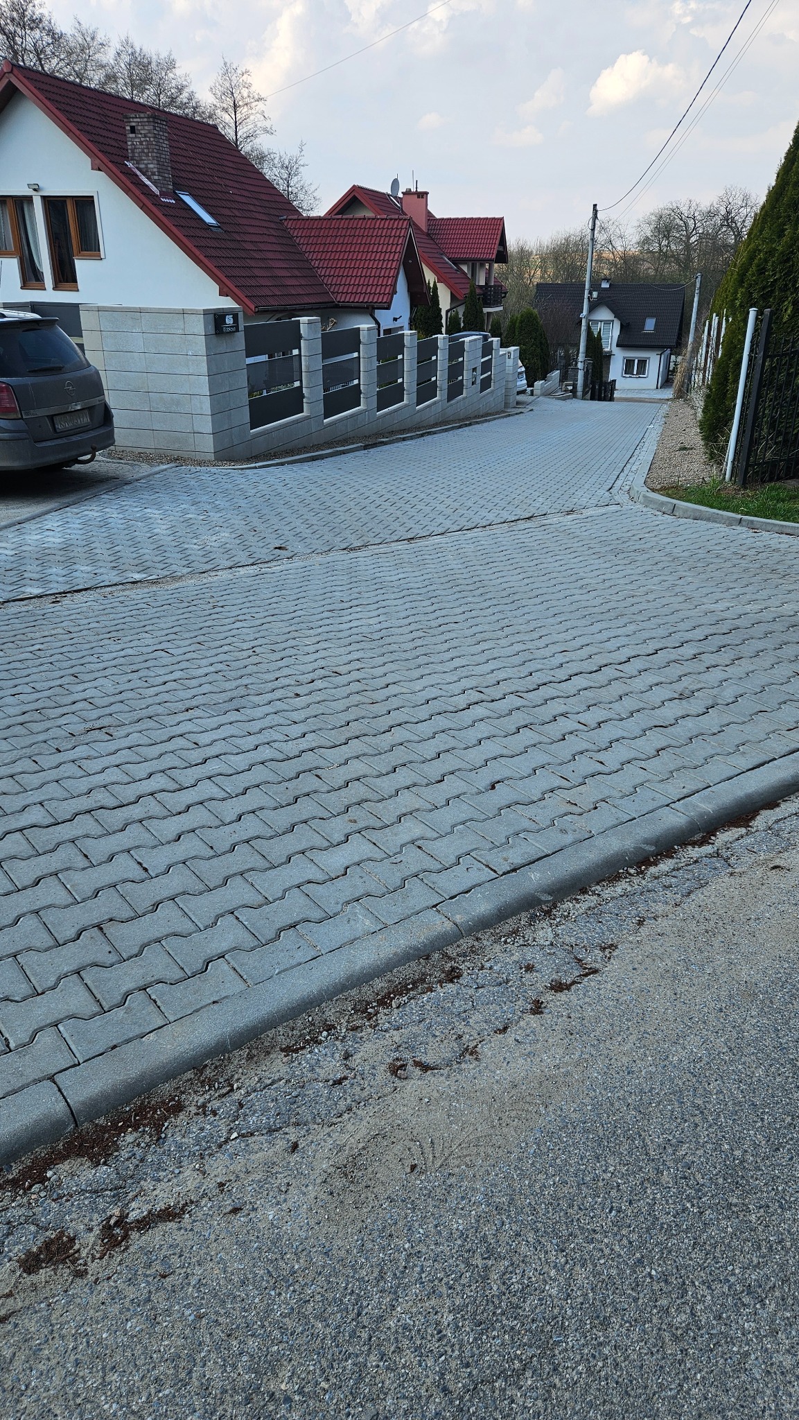 Szeroki kadr na ulicę w Sulechowie wyłożoną szarą kostką brukową w jodełkę, z widocznymi domami jednorodzinnymi i ogrodzeniami w tle.