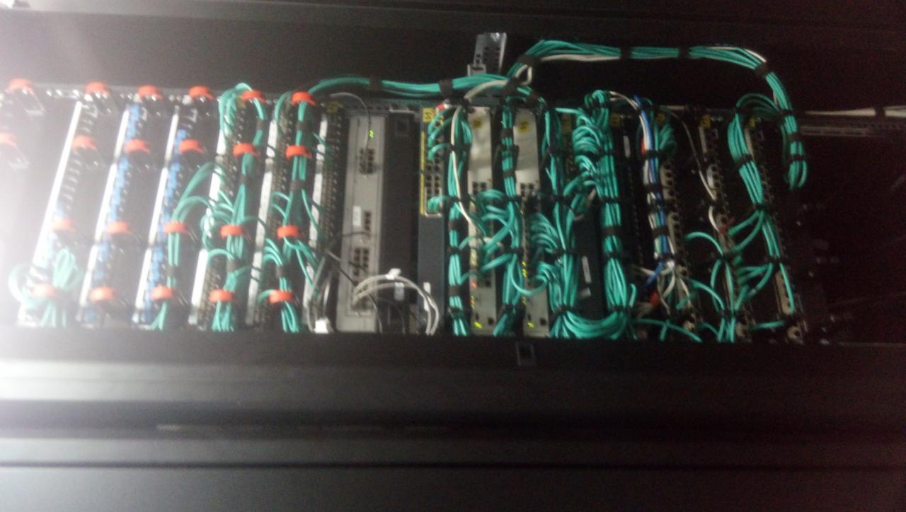 Serwerownia z uporządkowanymi kablami sieciowymi w kolorze turkusowym, spiętymi pomarańczowymi opaskami, widoczne diody sygnalizacyjne na urządzeniach.