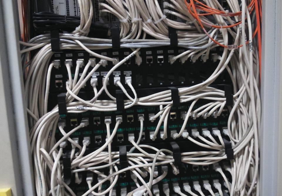 Patch panel z gęsto upakowanymi kablami sieciowymi, uporządkowanymi czarnymi opaskami zaciskowymi, widoczne oznaczenia na kablach.