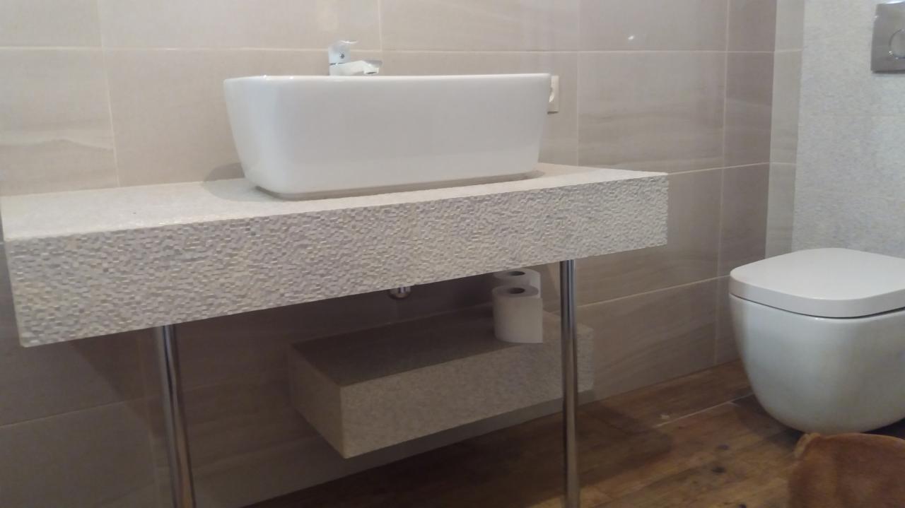 Nowoczesna łazienka z białą, prostokątną umywalką nablatową na blacie o chropowatej fakturze, wspartym na metalowych nogach, obok toaleta.