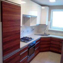 PPUH NIXSTYL - Nowoczesna kuchnia z białymi górnymi szafkami i dolnymi szafkami z ciemnego drewna, srebrne uchwyty, płyta gazowa i piekarnik, jasna podłoga, okno z białymi ramami.