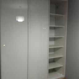 PPUH NIXSTYL - Biała szafa wnękowa z przesuwnymi, lustrzanymi drzwiami, częściowo otwarta, ukazująca półki. Widoczna podłoga z paneli.