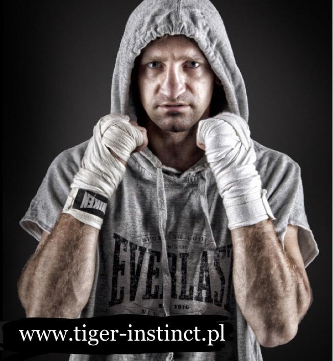 Mężczyzna w szarej bluzie z kapturem i owiniętych bandażami dłoniach, przygotowany do treningu sportów walki, z widocznym logo Everlast na bluzie i adresem strony internetowej w dolnej części kadru.