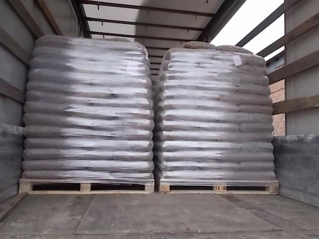 Dwa rzędy palet z workami pelletu, owinięte folią stretch, widoczne wewnątrz przestrzeni ładunkowej pojazdu.