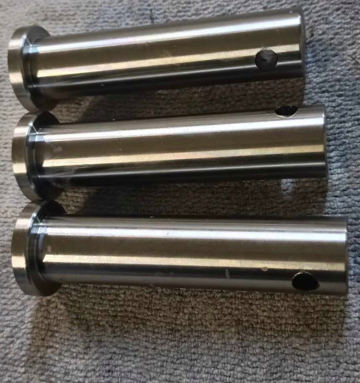 Trzy metalowe, cylindryczne elementy z kołnierzem i otworem, ułożone równolegle na szorstkiej powierzchni. Precyzyjna obróbka, widoczne refleksy światła.