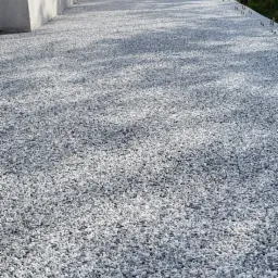 Biało-szary żwir na dachu budynku, widoczne elementy konstrukcyjne dachu, budynek w tle.