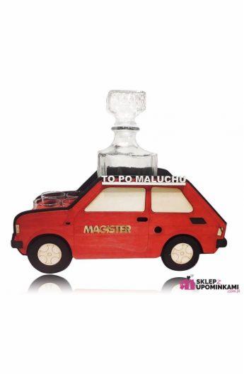 Karafka z kieliszkami w drewnianym stojaku w kształcie czerwonego samochodu z napisem 'Magister' i tekstem 'To po maluchu'.