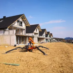 Montaż okien w szeregu domów jednorodzinnych w stanie surowym, widoczny dźwig pająk z przyssawkami do szyb.