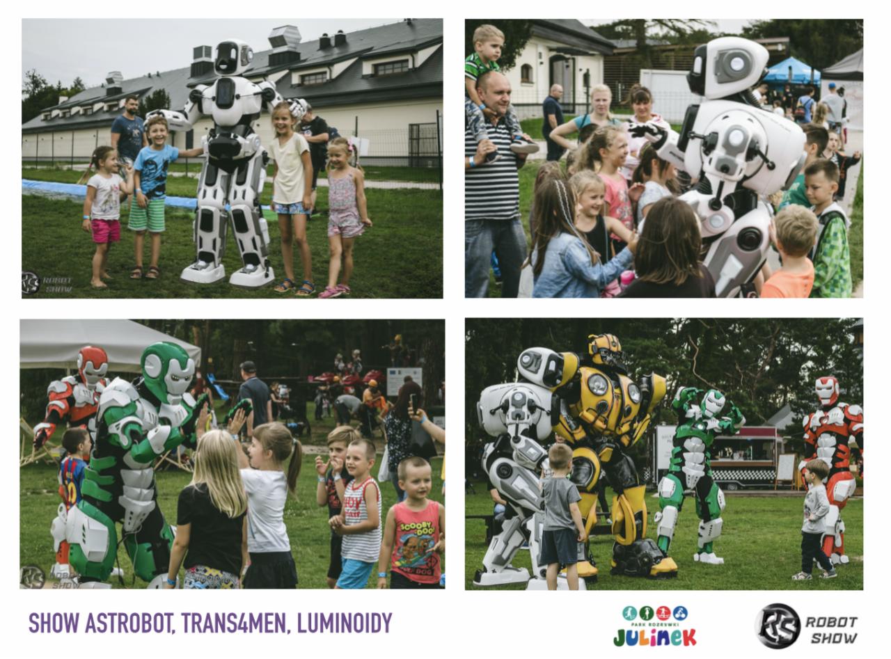 Animacje dla dzieci z robotami: Grupa dzieci pozuje z białym robotem w parku, inne roboty w kostiumach superbohaterów w tle, zabawa na świeżym powietrzu.