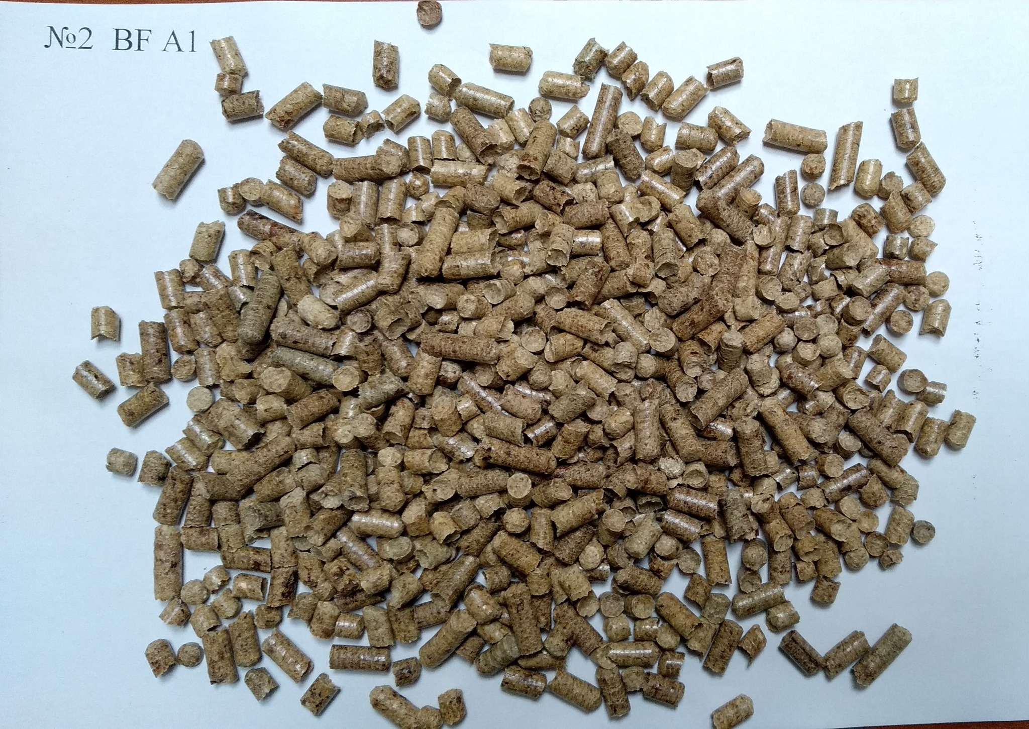 Jasnobrązowy pellet drzewny luzem na białym tle, widoczny napis 'No2 BF A1', produkt z Krakowa.