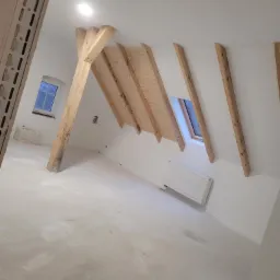 Poddasze po wykonaniu gładzi, widoczne drewniane elementy konstrukcyjne dachu, okno dachowe i grzejnik.