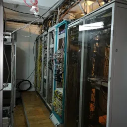 Serwerownia z widocznymi szafami rack, okablowaniem biegnącym po suficie i podłodze z drewnianych desek.