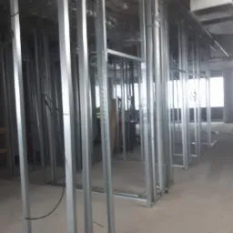 Metalowa konstrukcja szkieletowa ścian działowych w surowym stanie, widoczne przewody instalacyjne pod sufitem, przygotowanie do dalszych prac wykończeniowych.