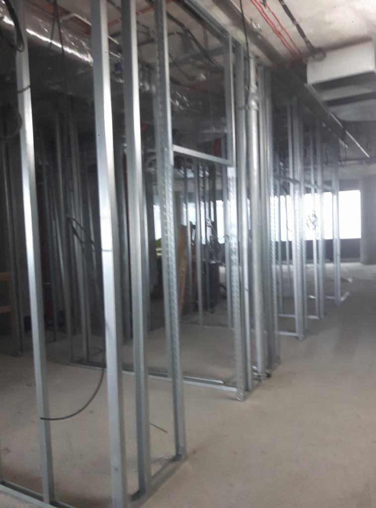 Metalowa konstrukcja szkieletowa ścian działowych w surowym stanie, widoczne przewody instalacyjne pod sufitem, przygotowanie do dalszych prac wykończeniowych.