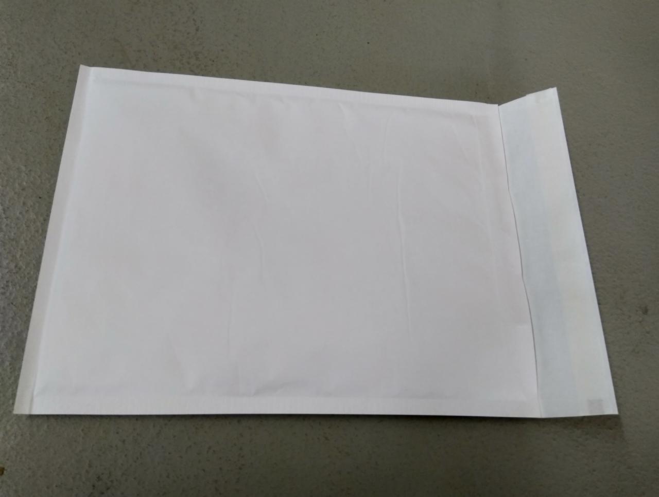 Pusta, biała koperta bąbelkowa leżąca na szarej powierzchni, gotowa do zaklejenia.