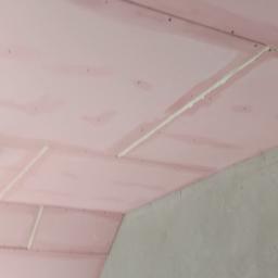 LAPIS HOME SP. Z O. O. - Różowe płyty kartonowo-gipsowe na suficie, z widocznymi łączeniami wypełnionymi masą szpachlową, oraz fragment surowej, szarej ściany w rogu pomieszczenia.