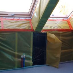 LAPIS HOME SP. Z O. O. - Przygotowanie poddasza do remontu: zabezpieczona folią ściana z oknem dachowym, widoczne fragmenty instalacji hydraulicznej i konstrukcji szkieletowej.