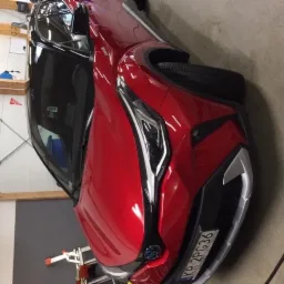 Czerwony samochód marki Toyota C-HR z widoczną tablicą rejestracyjną w hali warsztatowej, prawdopodobnie po umyciu.