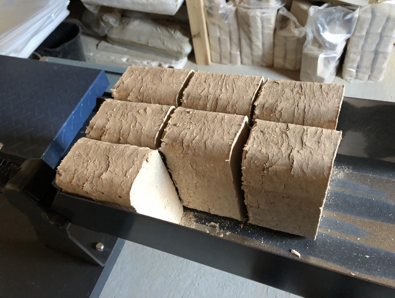 Ułożone rzędem, surowe kostki paliwa opałowego na metalowej konstrukcji, z widoczną strukturą włókien i jasnym przekrojem jednej kostki.