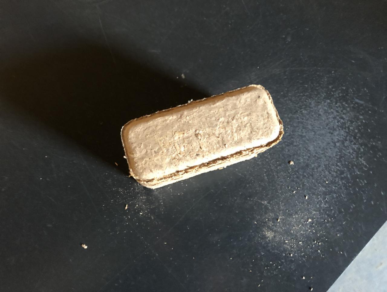 Pojedyncza kostka sprasowanych trocin na czarnym tle, widoczne drobne okruchy.