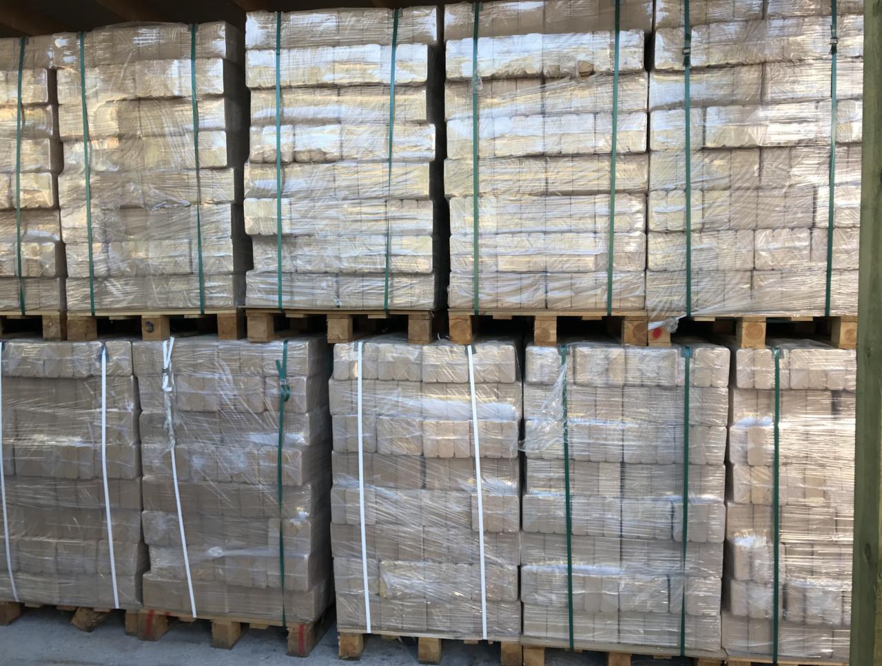 Sztaple palet z pakietami ułożonych kostek opału, owiniętych folią i spiętych taśmą, widoczne drewniane palety.