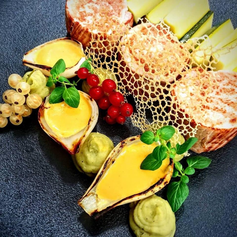 Elegancko podane danie z grillowaną cebulą wypełnioną sosem, plastrami mięsa z dekoracją z jadalnej siatki, zielonym puree, czerwoną i białą porzeczką, ozdobione świeżymi listkami ziół na czarnym...