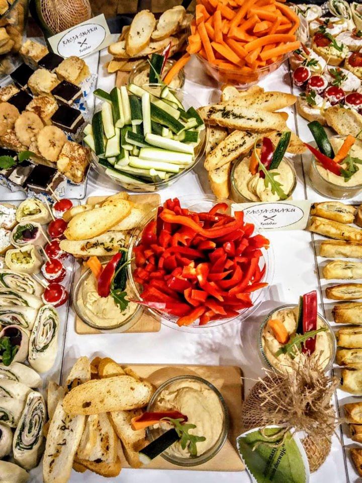 Bogaty wybór przekąsek cateringowych: kolorowe warzywa w słupkach, mini kanapeczki, roladki szpinakowe i brownie na białym stole.