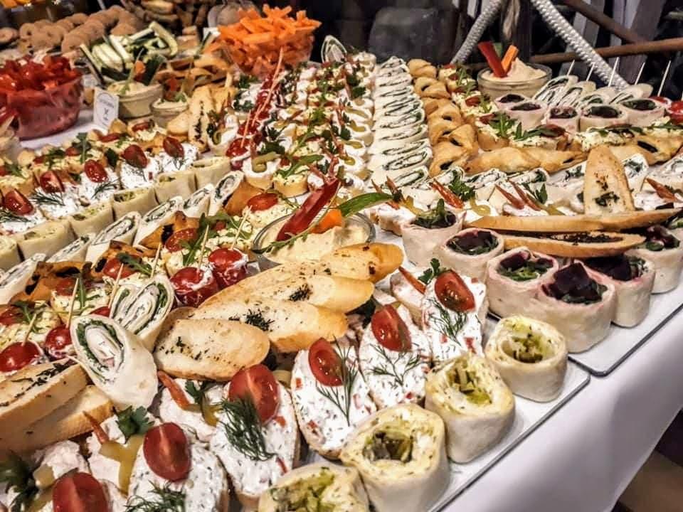 Bogato zastawiony stół cateringowy z różnorodnymi przekąskami: roladki z tortilli, kanapki z pastami, warzywa i dipy, tworzące apetyczną kompozycję.