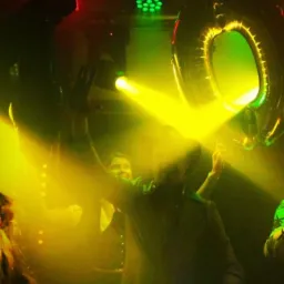 Osoby na parkiecie w stroboskopowym oświetleniu, dekoracja w postaci balonu w kształcie cyfry zero, widoczne elementy nagłośnienia i oświetlenia scenicznego.