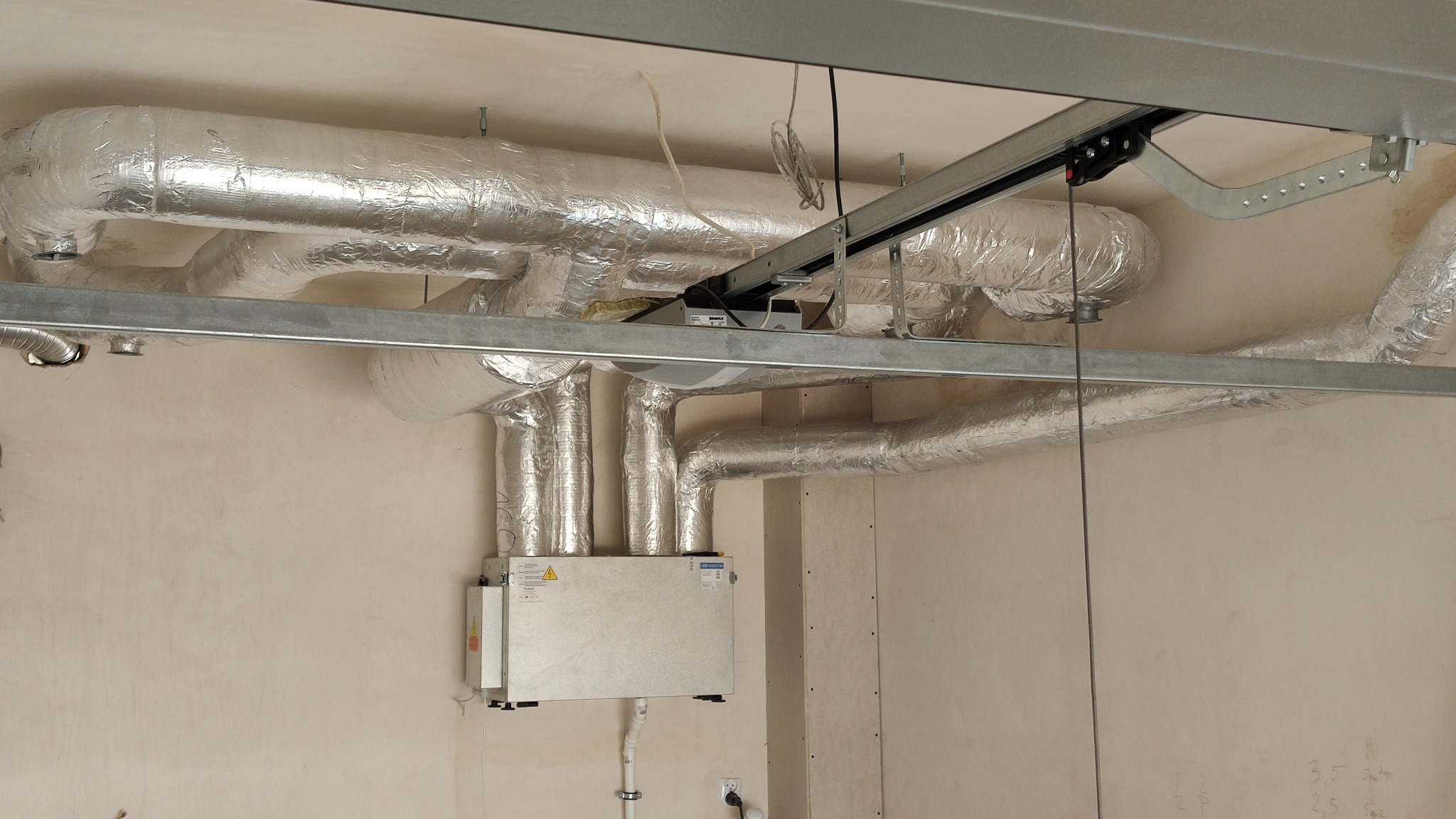 Centrala wentylacyjna z rekuperacją zamontowana pod sufitem, z widocznymi izolowanymi przewodami wentylacyjnymi i elementami mocującymi do sufitu.