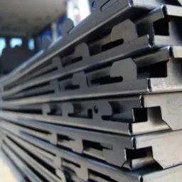 Stos wygiętych, metalowych profili z charakterystycznymi wycięciami, prawdopodobnie element&oacute;w konstrukcyjnych ogrodzenia panelowego, ułożonych wewnątrz pojazdu.