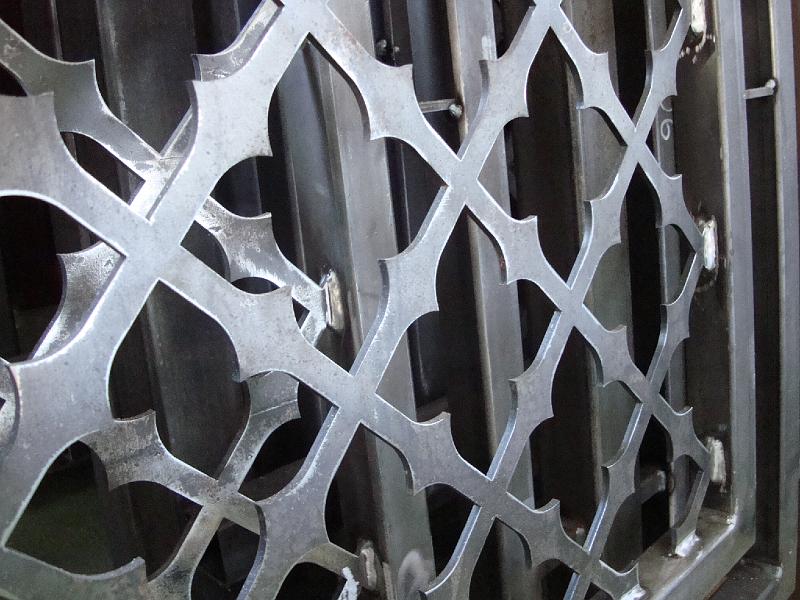 Metalowy element dekoracyjny wycinany laserowo, z powtarzalnym wzorem krzyży i łuków, świeżo po obróbce, widoczne ślady spawania.