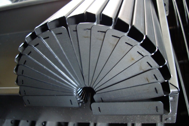 Metalowe profile z wyciętymi otworami ułożone wachlarzowo na prasie krawędziowej CNC.