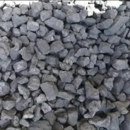 Kupa antracytowych bryłek ekogroszku o nieregularnych kształtach, z widocznymi drobnymi refleksami światła na powierzchni.