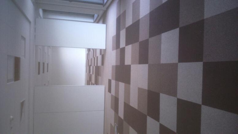 Ściana z dekoracyjnym wzorem kwadratów w odcieniach brązu i beżu, widok z boku, fragment białych drzwi po lewej stronie.
