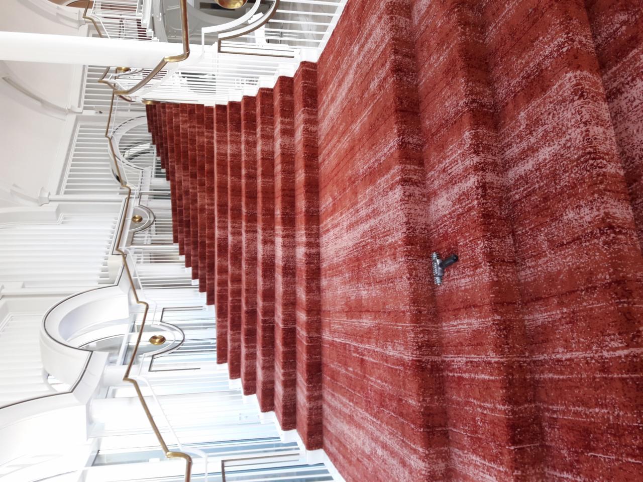 Czerwona wykładzina dywanowa na schodach w nowoczesnym, białym wnętrzu z metalowymi balustradami, widok z dołu.
