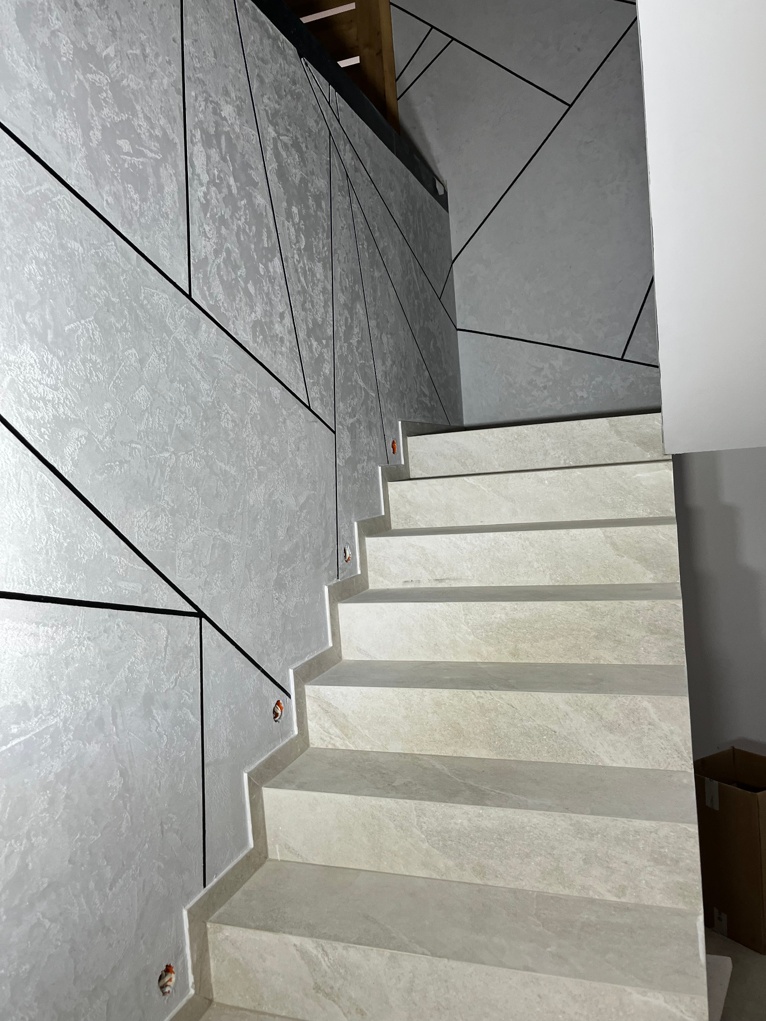 Wykończone schody z okładziną imitującą kamień, ściany z dekoracyjną szpachlą w odcieniach szarości, geometryczne wzory z czarnych listew.